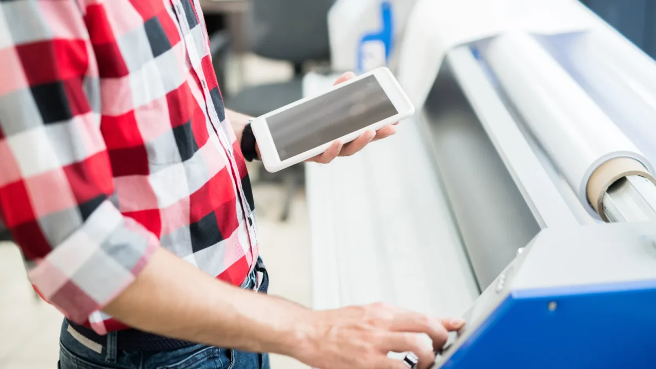 Imprimeur pilotant une presse numérique depuis une tablette dans son atelier