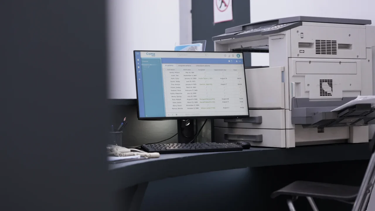 Poste informatique affichant un logiciel de gestion à côté d'un système d'impression